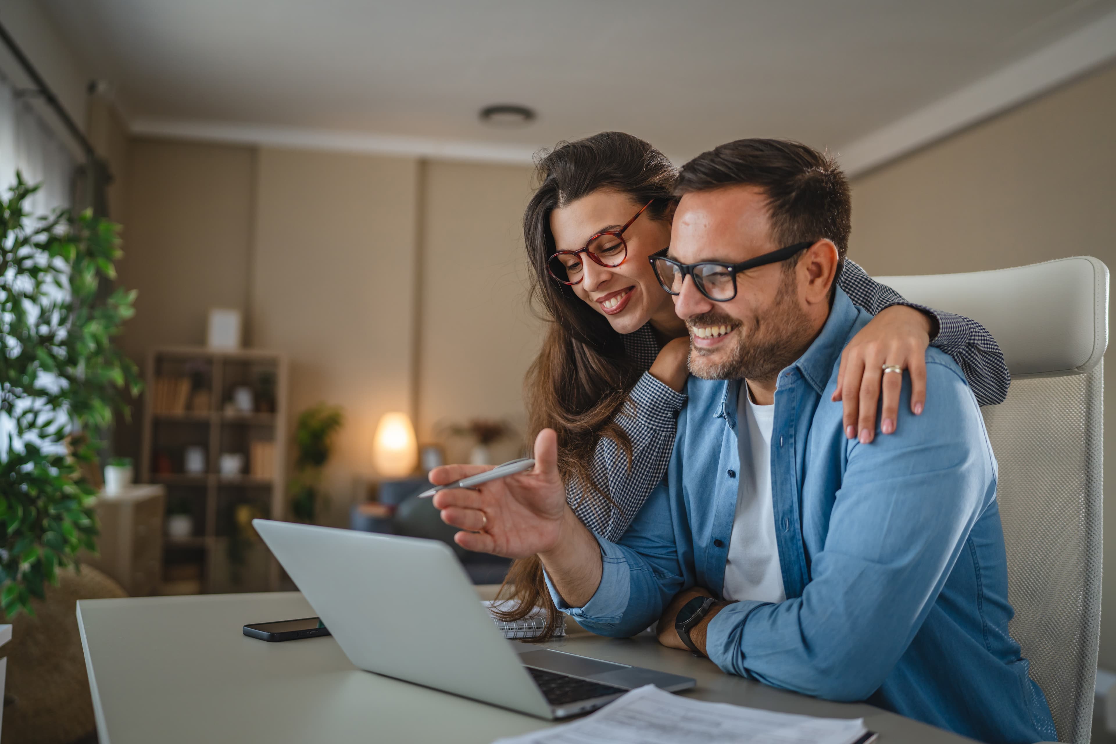 A couple planning together at home while looking at a laptop and paperwork.